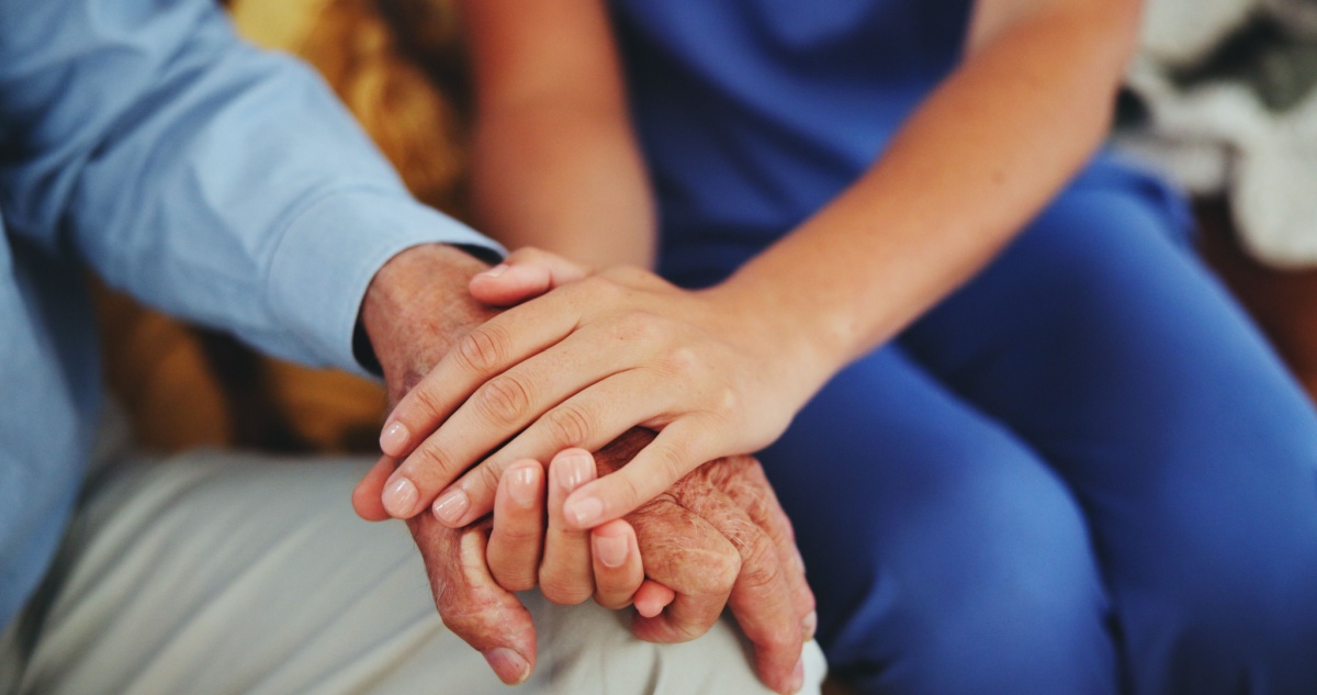 an in-home caregiver holding the hand of her elderly, male patient